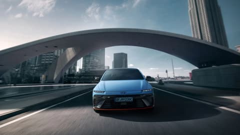 IONIQ 6 N преминава под аркадния мост, демонстрирайки своя модерен дизайн на фона на градския пейзаж.