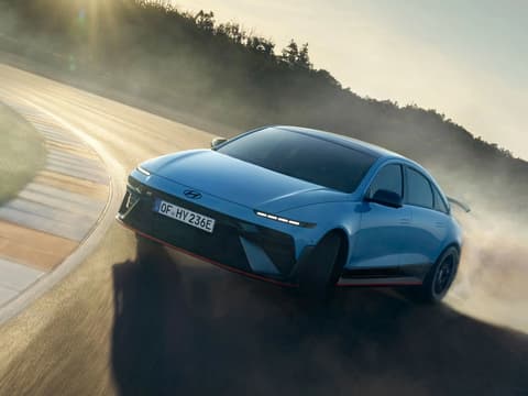 Hyundai IONIQ 6 N дрифтира на състезателна писта, издигайки облаци прах в динамична позиция по време на движение.