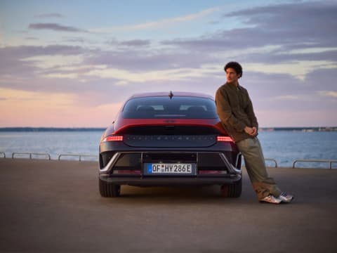 Мъж, облегнат на Hyundai IONIQ 6 N Line, паркиран до океана.