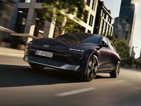 HYUNDAI IONIQ 6 в движение по градска улица, заснет от нисък заден ъгъл, подчертаващ скоростта, динамиката и модерния дизайн.