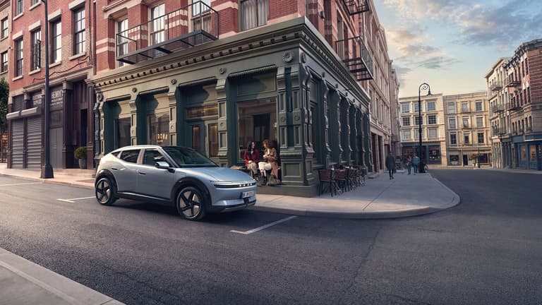 Hyundai IONIQ 3 EV, паркиран на градска улица, с две жени, седнали на стъпалата до него.