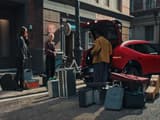 Червен Hyundai IONIQ 3, страничен изглед, паркиран на градска улица с багаж до автомобила.