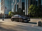 Hyundai IONIQ 6 електрически седан, сниман в профил, паркиран на градска улица с небостъргачи.