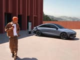 Мъж се отдалечава от Hyundai IONIQ 6 с чаша кафе, докато колата се зарежда.