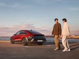 Мъж и жена вървят край задната част на паркиран Hyundai IONIQ 6 до брега.