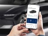 Човек гледа смартфон с приложението myHyundai. На заден план е паркиран Hyundai IONIQ 6 на улицата.