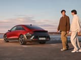 Мъж и жена минават покрай червен Hyundai IONIQ 6 N Line, паркиран до океана.