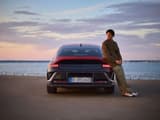 Мъж, облегнат на Hyundai IONIQ 6 N Line, паркиран до океана.