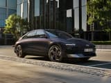 HYUNDAI IONIQ 6 паркиран на тиха градска улица пред модерни стъклени сгради, показващ елегантния си страничен профил и отличителна визия.