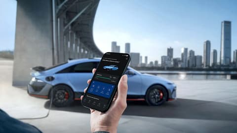 Hand holding smartphone displaying Hyundai IONIQ 6 N charging status with car and city skyline.