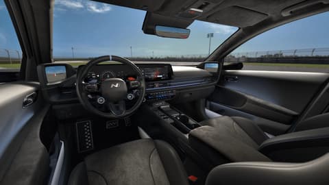 Interior view of Hyundai IONIQ 6N showing a driver-focused cockpit, dual displays and sporty seating on a race track.