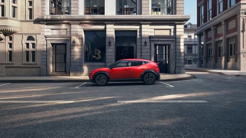 Red Hyundai IONIQ 3 parked side view on a street, with a gallery behind the car.
