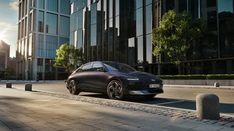 Hyundai IONIQ 6 електрически седан, заснет отстрани, паркиран на градска улица с високи сгради.