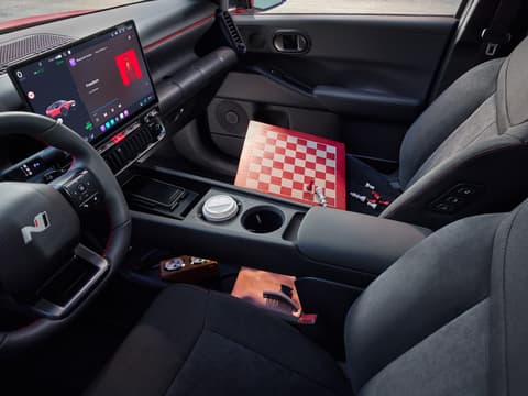 Изглед към интериора на Hyundai IONIQ 3 с човек на предната пасажерска седалка, показваща централната конзола и поставки за чаши.