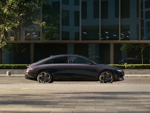 Hyundai IONIQ 6 електрически седан, сниман от нивото на улицата, паркиран с модерна сграда на заден план.