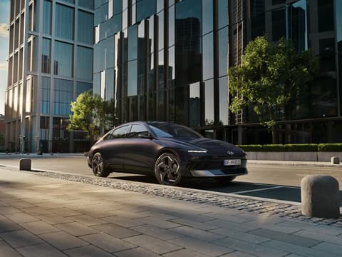 Hyundai IONIQ 6 електрически седан, сниман в профил, паркиран на градска улица с небостъргачи.