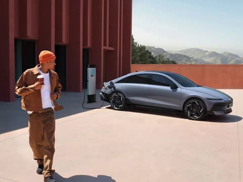 Мъж се отдалечава от Hyundai IONIQ 6 с чаша кафе, докато колата се зарежда.