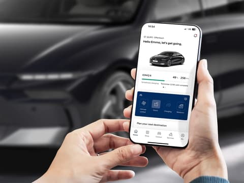 Човек гледа смартфон с приложението myHyundai. На заден план е паркиран Hyundai IONIQ 6 на улицата.
