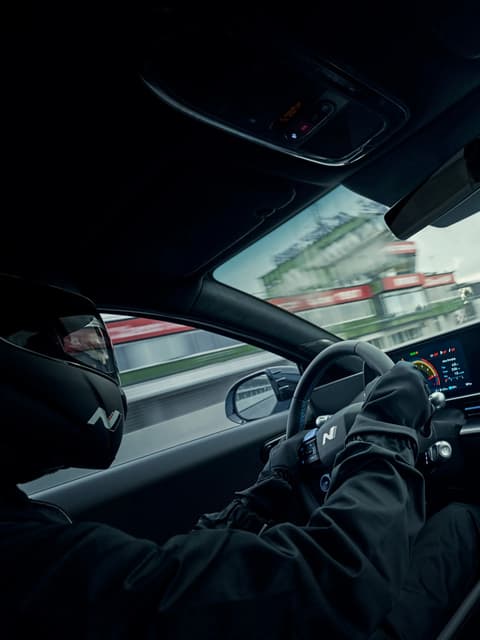 Шофьор с ръкавици управлява IONIQ 6 N, акцентирайки върху спортния кокпит и табло.