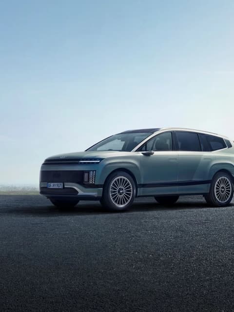 Hyundai IONIQ 9 е паркиран върху настилка под ясно небе, открояващ елегантните си дизайнерски акценти като тесни фарове и големи джанти.