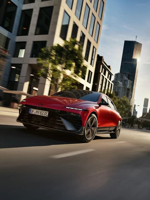 Червен Hyundai IONIQ 6 N Line, движещ се из модерен градски пейзаж.