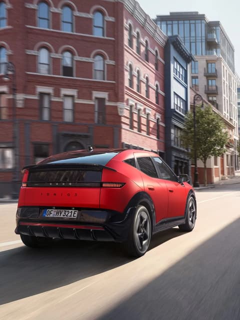 Red Hyundai IONIQ 3 driving down the urban street.