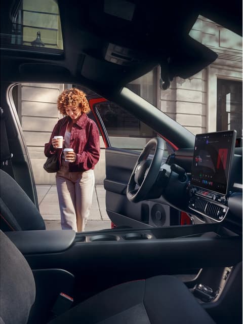 A woman holding cups in both hands walking into Hyundai IONIQ 3.