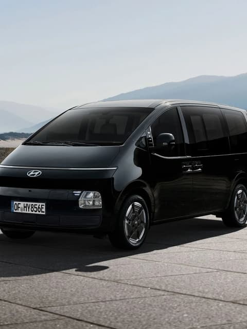 Hyundai STARIA Electric, паркиран на открито, с планински пейзаж на заден план, видян под преден тричетвърти ъгъл.