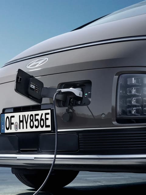 Близък план на предната част на Hyundai STARIA Electric с отворен порт за Зареждане и включен кабел за зареждане.
