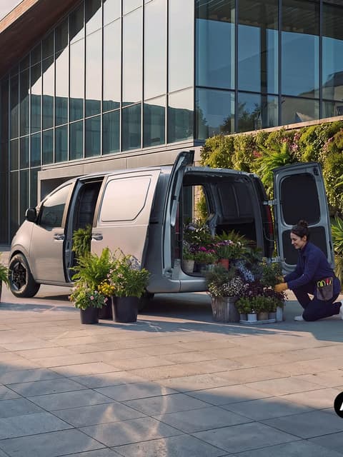 Жена разтоварва саксии с растения от Hyundai STARIA Cargo пред модерна сграда.