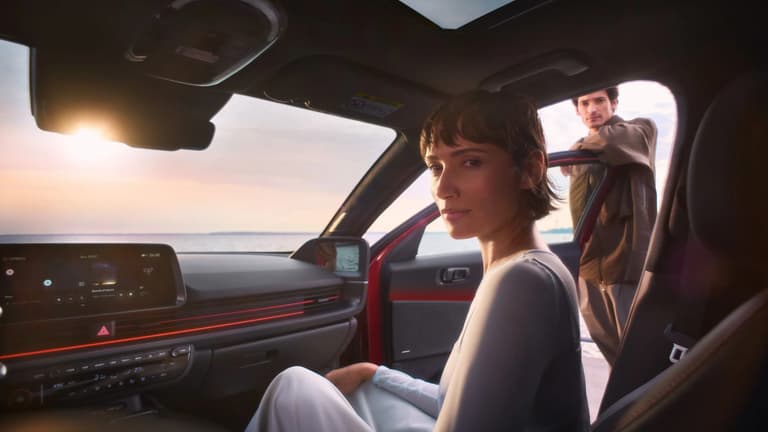 Жена на предната пътническа седалка на Hyundai IONIQ 6, докато мъж се обляга на отворената врата.