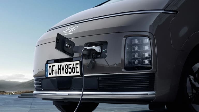 Близък план на предната част на Hyundai STARIA Electric с отворен порт за зареждане и включен кабел.
