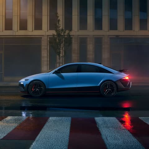 Страничен изглед на Hyundai IONIQ 6 N, паркиран в градска среда нощем, със светлини на мокър асфалт.