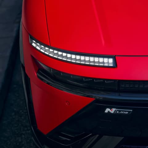 Червен Hyundai IONIQ 3, предна част с тясна LED светлинна лента и знак N Line върху скулптурираната каросерия.