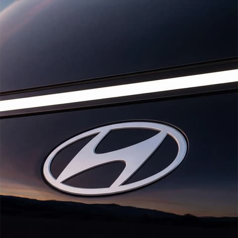 Детайл на предната емблема на Hyundai STARIA Electric с LED светлинна лента при залез.