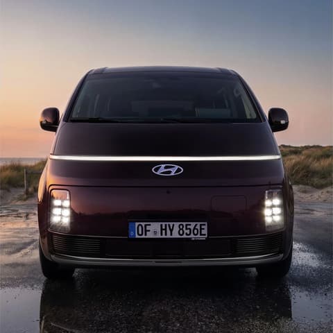 Изглед отпред на Hyundai STARIA Electric със светещи LED светлини при залез.