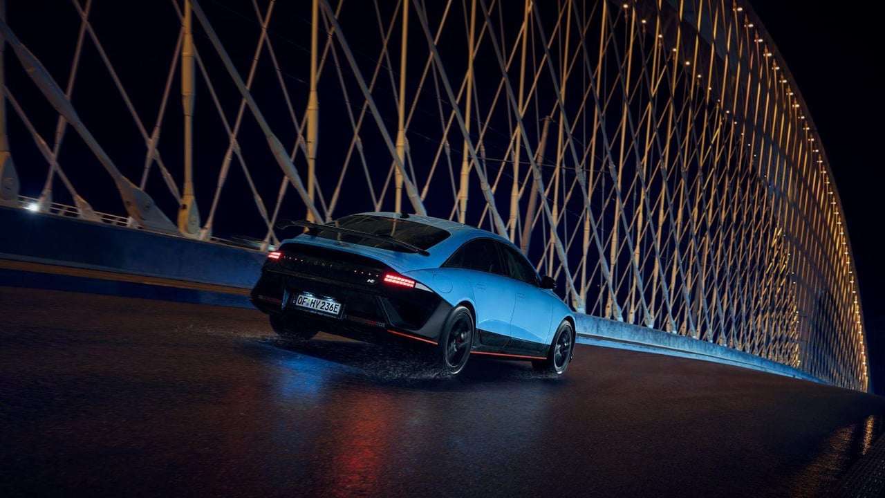 A Hyundai IONIQ 6 N drives across a bridge at night, surrounded by illuminated architectural elements.