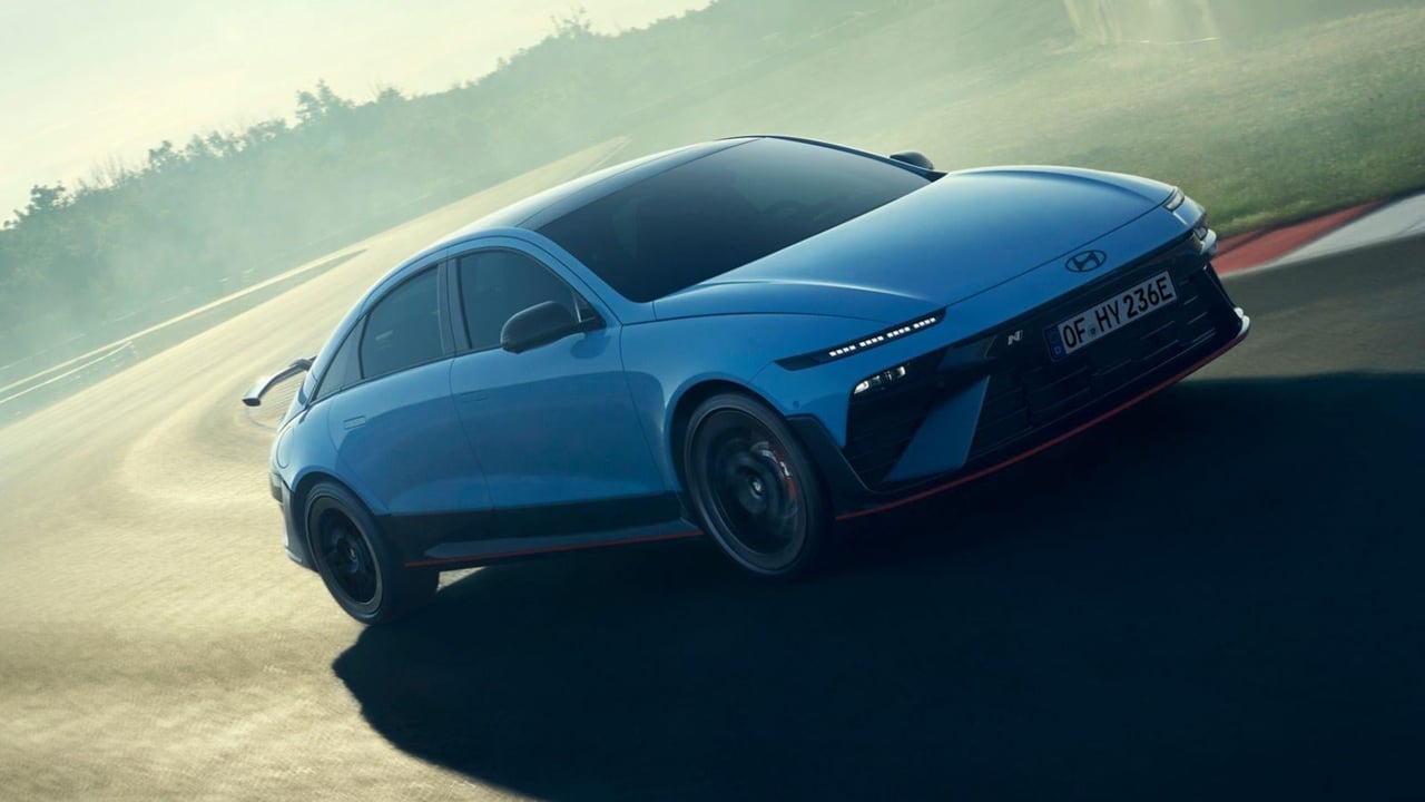 A Hyundai IONIQ 6 N powers through a track corner, showcasing its performance in a misty environment.