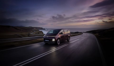 Hyundai STARIA Electric шофира по крайбрежен път при залез.