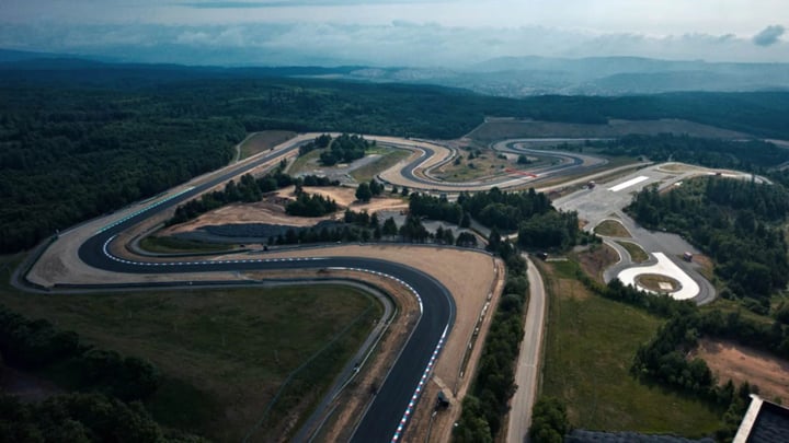 Aerial view of a winding racetrack surrounded by lush greenery, showcasing the layout and curves of the course.